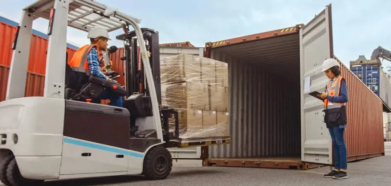 Supervisor watching a forklift load a wrapped pallet into a shipping container