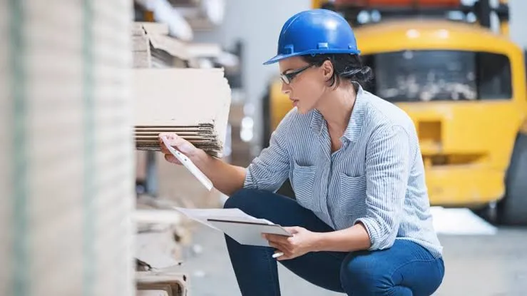 Warehouse inspector in a hard hat checking carton stock before an export shipment