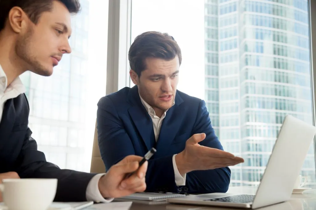 Two buyers building a supplier compliance register on a laptop beside printed documents in an office