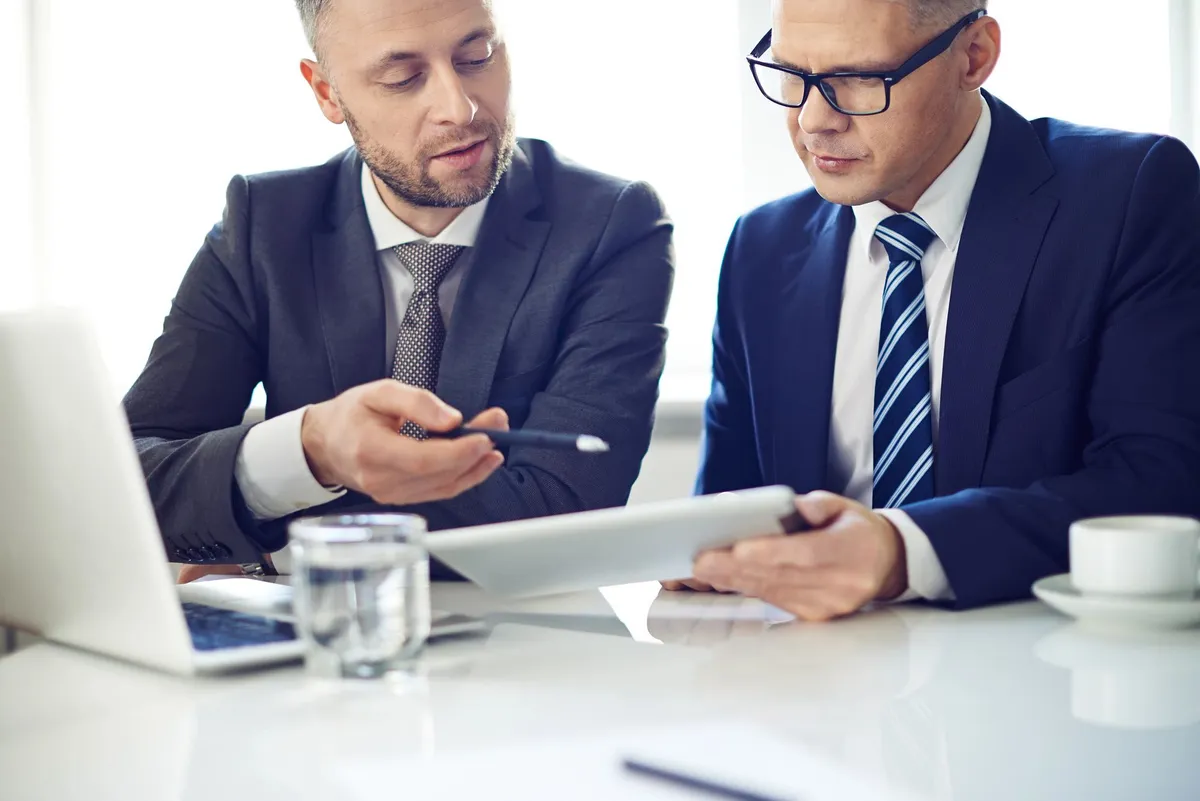 Two procurement managers reviewing supplier documents and a laptop together before a factory compliance audit