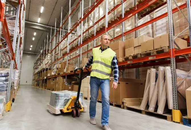 A warehouse worker moving a pallet of stock through a distribution aisle